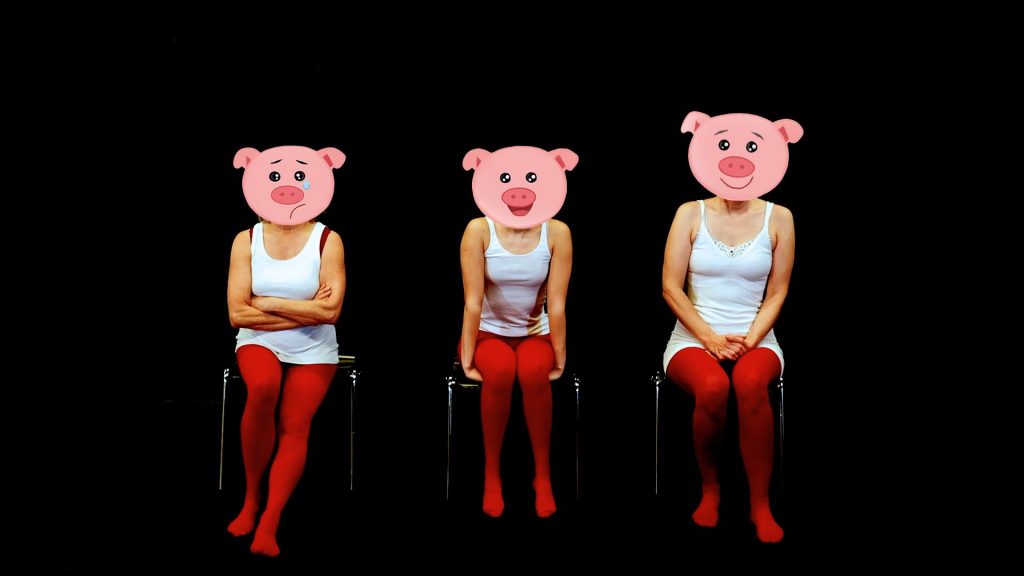 Drei Schauspielerinnen sitzen vor schwarzem Hintergrund. Ihre Gesichter sind von Schweine-Emojis verdeckt. Sie tragen weiße Tacktops und rote Strumpfhosen.